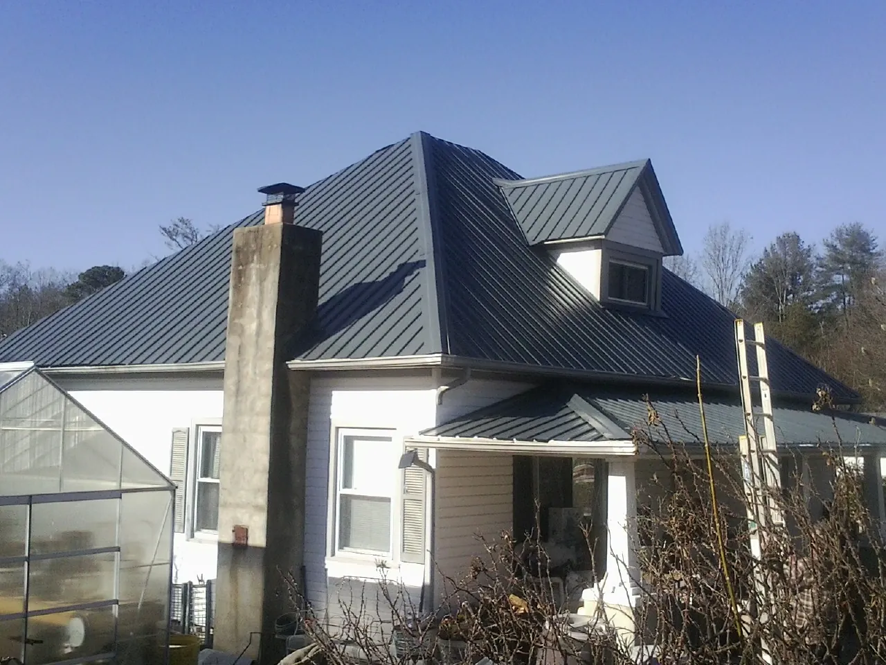 Dark blue standing seam metal roof on a white farmhouse with dormer — Slate & Tile Roof Repair by Roofing Brothers in Helenwood