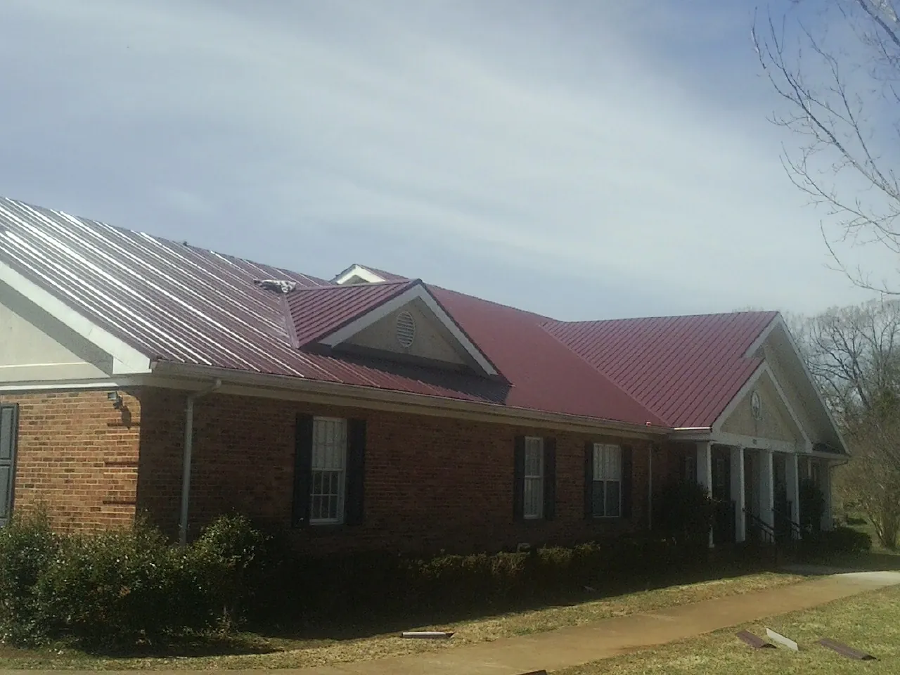 Red metal roof with gabled entries on a long brick building, from a Hail Damage Roof Repair job in Helenwood