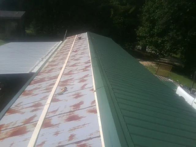 Old rusted panels beside newly installed green metal roofing — Wind Damage Roof Repair by Roofing Brothers in Helenwood