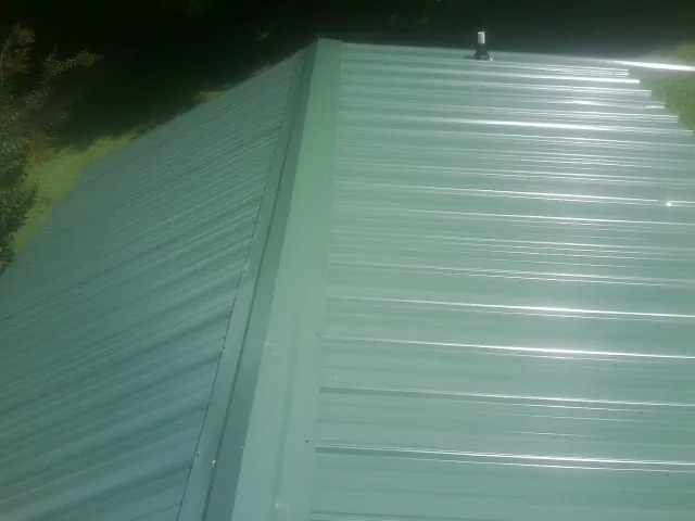 New green metal panels meeting at the ridge of a roof — Flat Roof Repair work by our crew in Helenwood