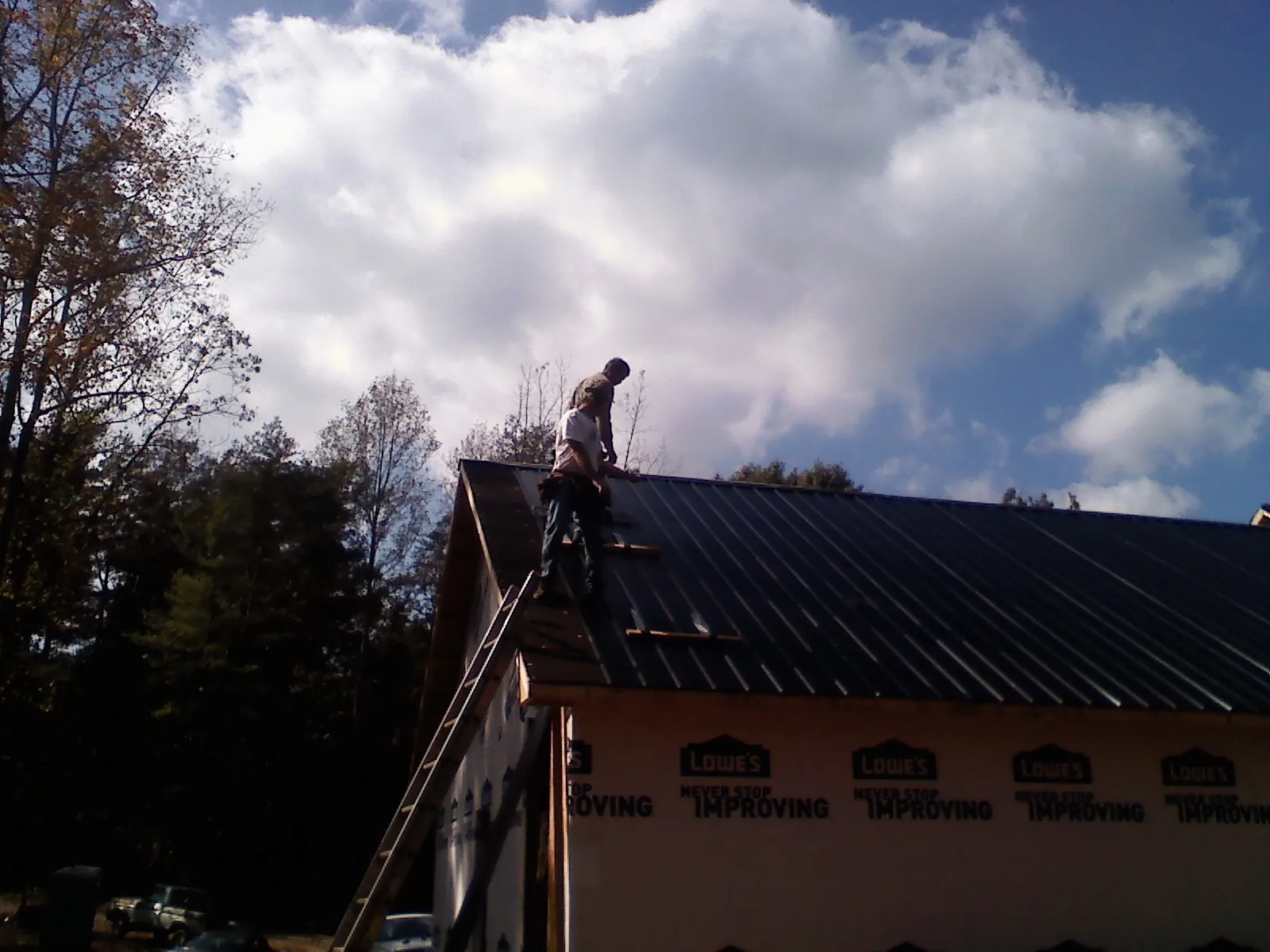 Roofer fastening dark metal panels high against a cloudy sky, from a Roof Inspection job in Helenwood