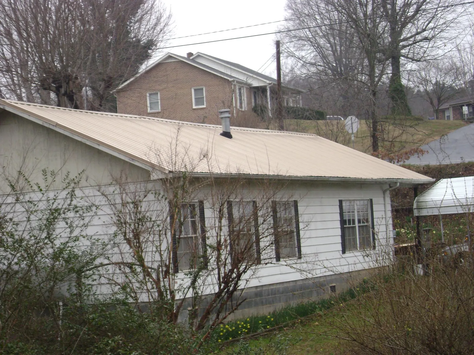 Tan metal roof on a white sided house set into a hillside — Commercial Roofing by Roofing Brothers in Helenwood