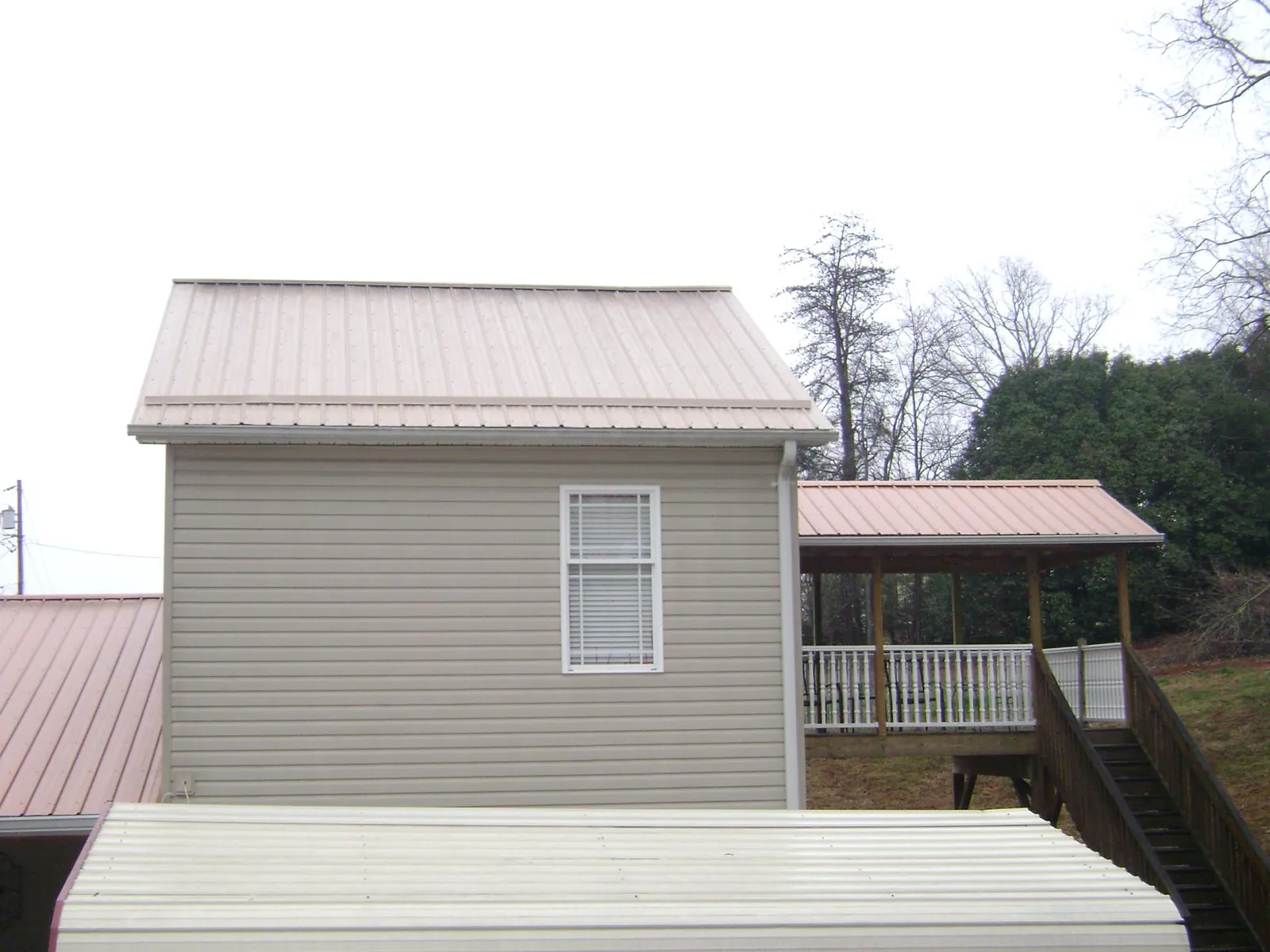 Tan metal roofs on a two story addition and attached porch, from a Roof Replacement job in Helenwood